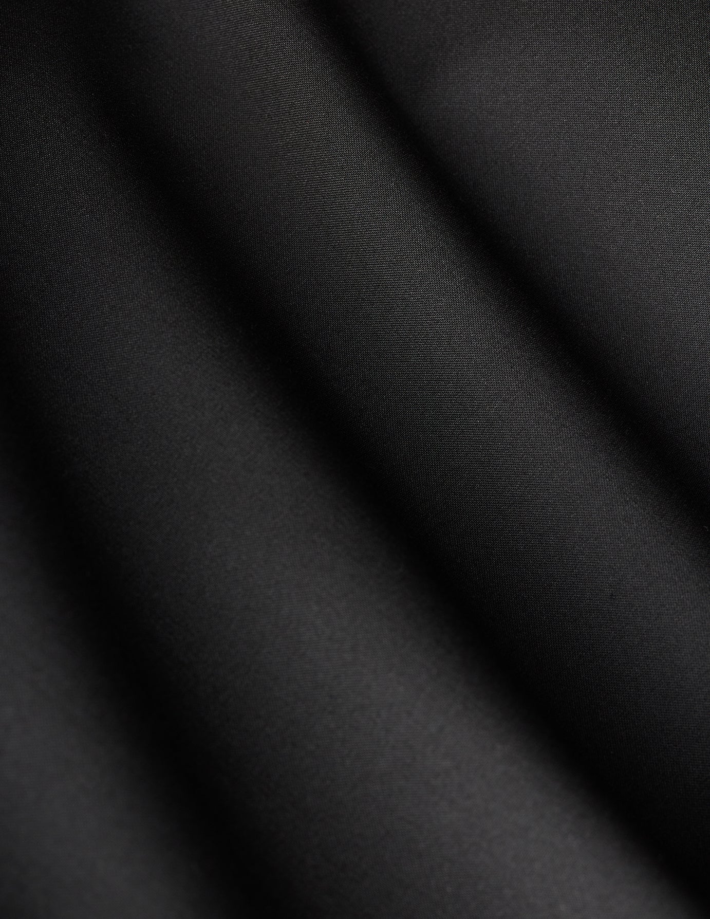 Närbild på dambyxan Avira Pants Wide Black med diagonala veck i tyget i en minimalistisk skandinavisk design.